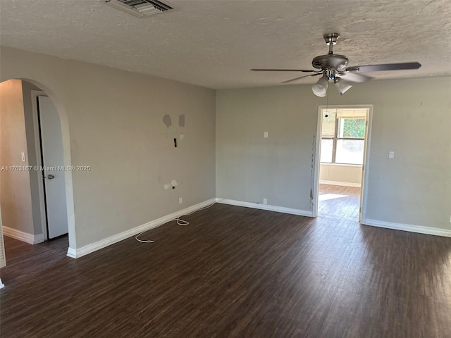 spare room with visible vents, arched walkways, baseboards, ceiling fan, and dark wood-style flooring