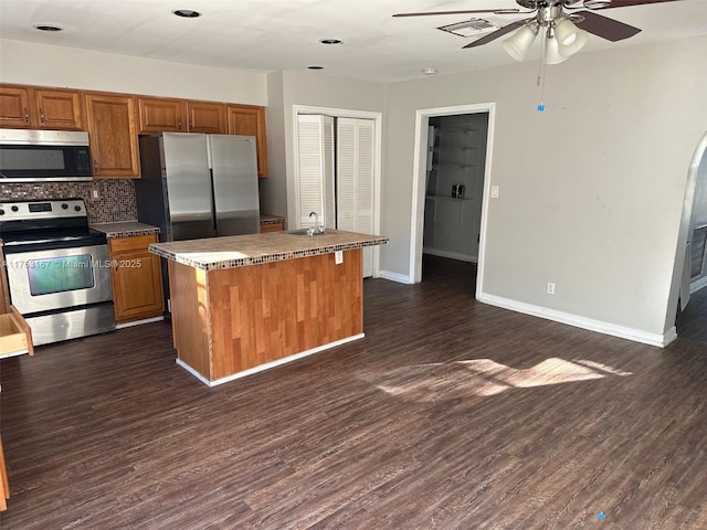 kitchen featuring backsplash, dark wood finished floors, appliances with stainless steel finishes, brown cabinetry, and ceiling fan