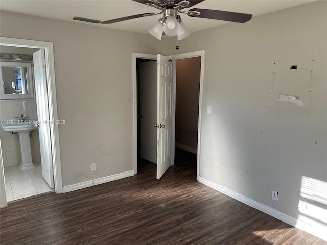 unfurnished bedroom with ensuite bath, wood finished floors, and baseboards