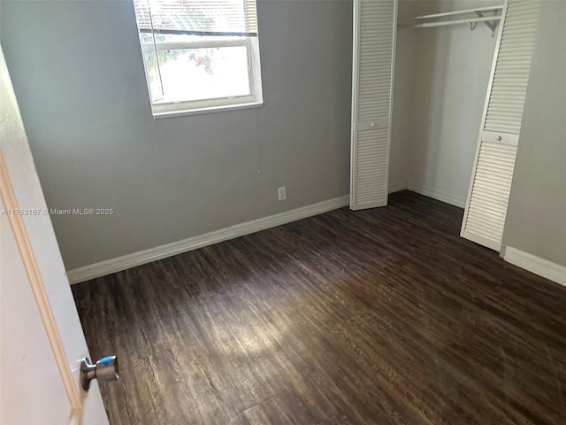 unfurnished bedroom with a closet, baseboards, and dark wood-type flooring