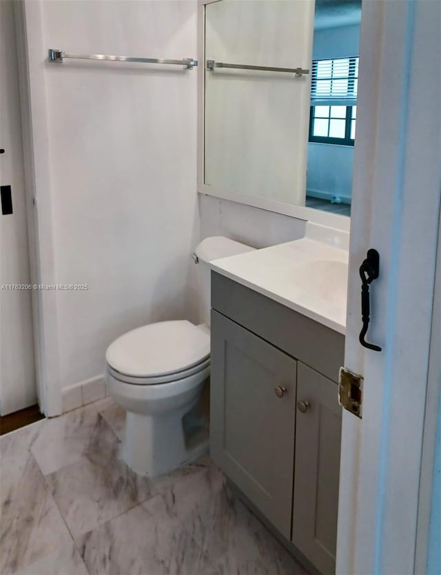 half bath featuring marble finish floor, toilet, and vanity