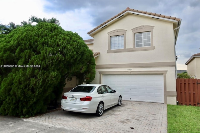 view of front of house with fence, a tiled roof, stucco siding, decorative driveway, and a garage