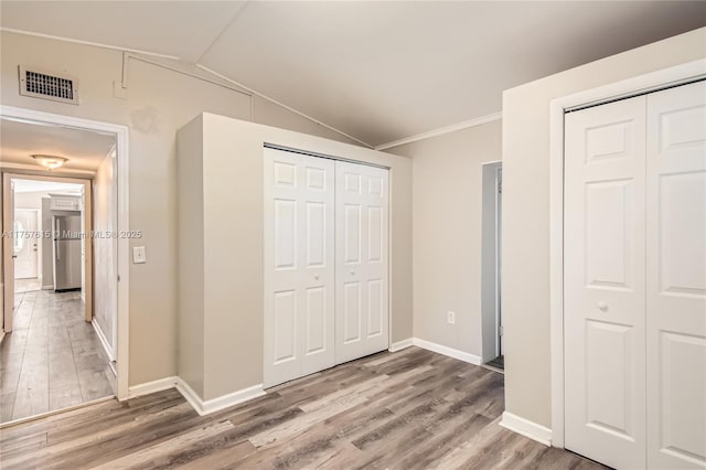 unfurnished bedroom featuring vaulted ceiling, wood finished floors, visible vents, and freestanding refrigerator