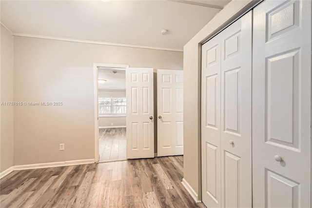 unfurnished bedroom featuring crown molding, baseboards, light wood-type flooring, and a closet