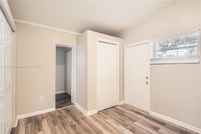 unfurnished bedroom featuring light wood-type flooring, a closet, baseboards, and vaulted ceiling