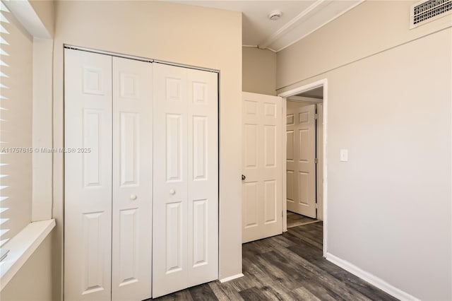 unfurnished bedroom with visible vents, baseboards, ornamental molding, dark wood-style floors, and a closet