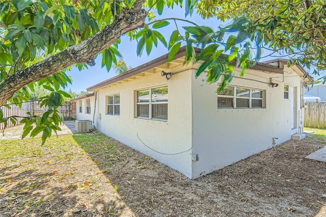 view of home's exterior featuring stucco siding, central AC, and fence