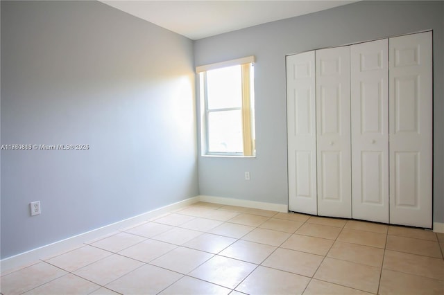 unfurnished bedroom featuring light tile patterned floors, baseboards, and a closet