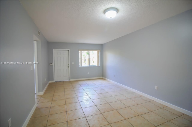 empty room featuring light tile patterned floors, visible vents, baseboards, and a textured ceiling