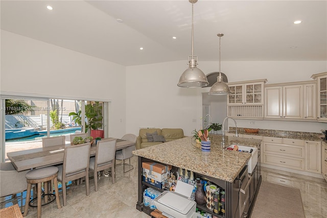 kitchen with glass insert cabinets, a center island with sink, light stone counters, cream cabinets, and a sink