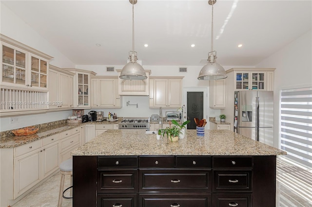 kitchen featuring visible vents, cream cabinetry, a kitchen island with sink, range with gas stovetop, and stainless steel fridge