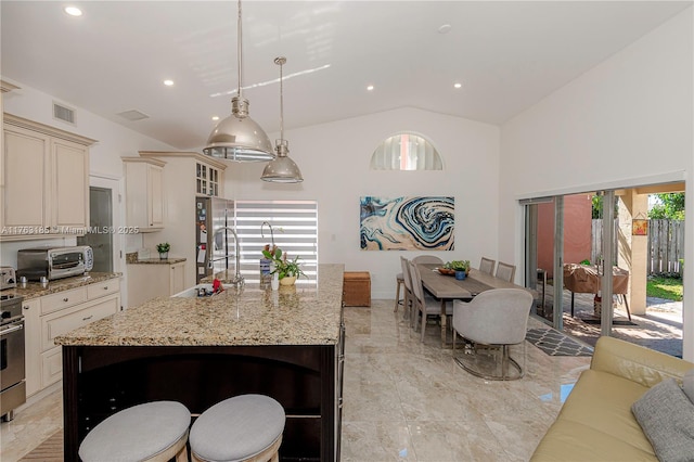 kitchen featuring visible vents, vaulted ceiling, light stone counters, cream cabinets, and stainless steel appliances