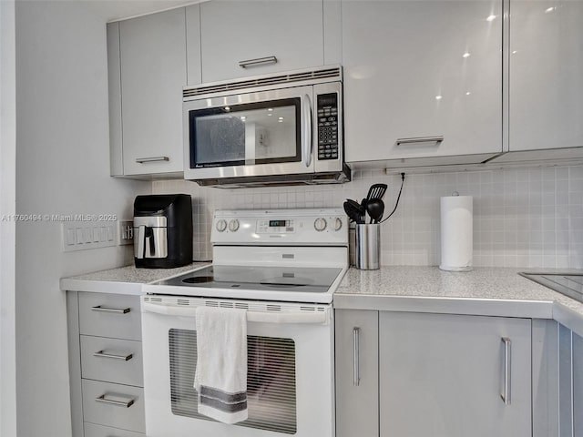 kitchen with stainless steel microwave, white electric stove, light countertops, and decorative backsplash