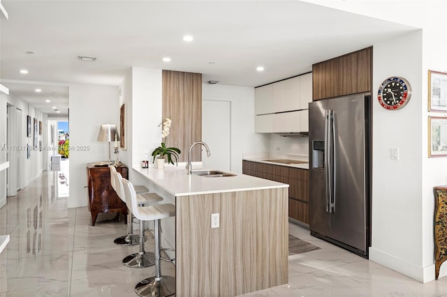 kitchen featuring stainless steel fridge with ice dispenser, a kitchen breakfast bar, marble finish floor, modern cabinets, and a sink