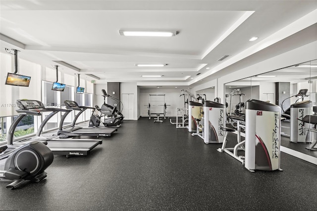 exercise room with a tray ceiling, recessed lighting, and visible vents