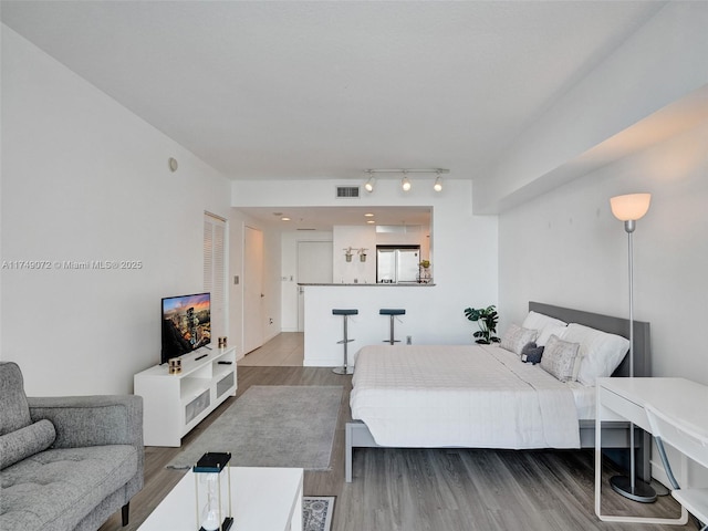 bedroom featuring visible vents, wood finished floors, rail lighting, and freestanding refrigerator