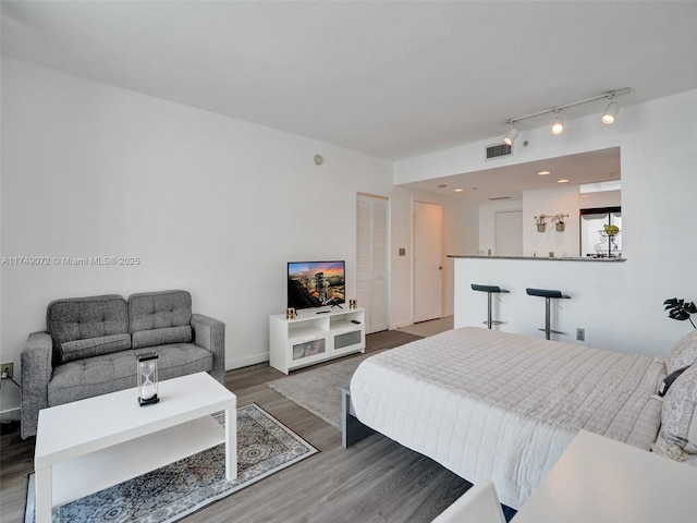 bedroom featuring visible vents, rail lighting, baseboards, and wood finished floors