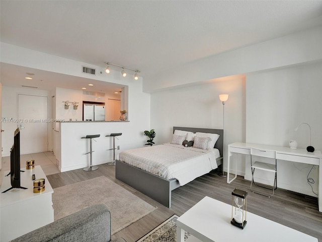 bedroom with visible vents, wood finished floors, freestanding refrigerator, rail lighting, and baseboards