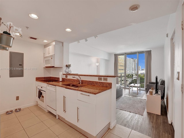 kitchen with a wall of windows, white appliances, a peninsula, electric panel, and a sink