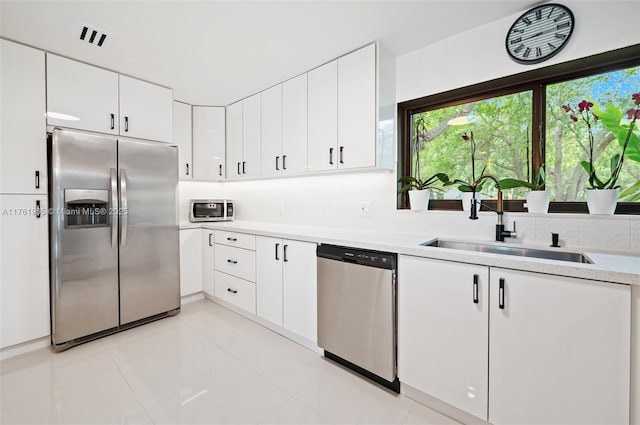 kitchen featuring backsplash, light countertops, appliances with stainless steel finishes, white cabinets, and a sink