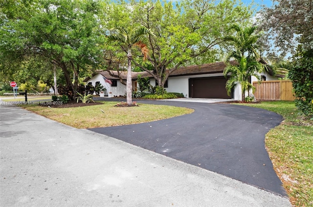single story home with aphalt driveway, an attached garage, a front lawn, and fence