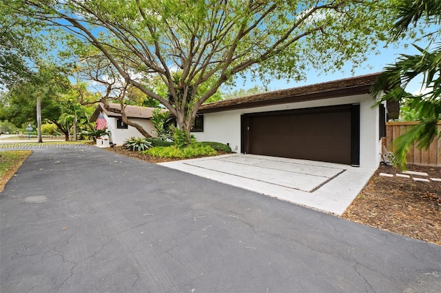 ranch-style home featuring an attached garage, fence, driveway, and stucco siding