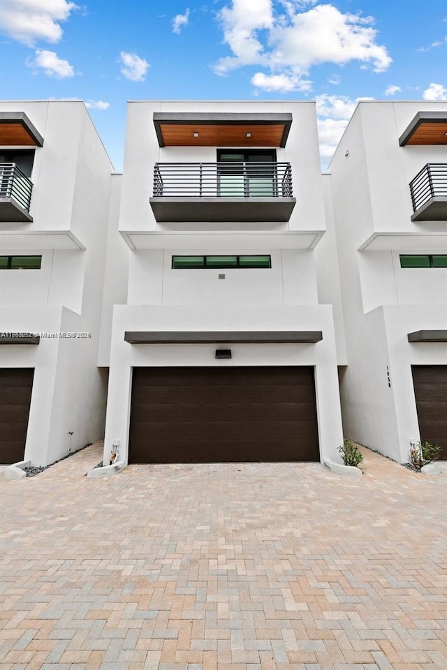 contemporary house featuring a garage, decorative driveway, a balcony, and stucco siding