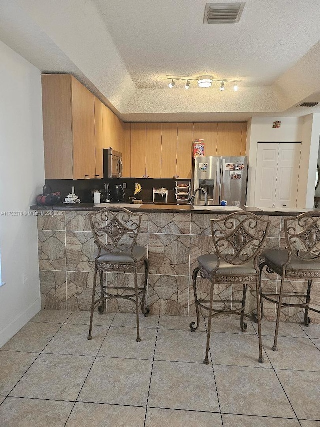 kitchen with a breakfast bar area, visible vents, stainless steel appliances, a textured ceiling, and dark countertops