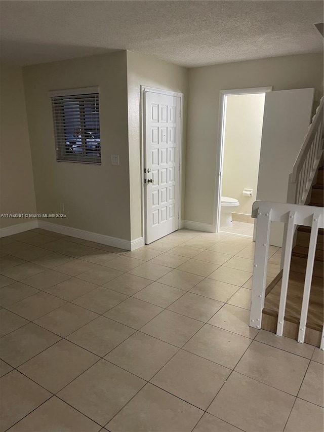 interior space featuring light tile patterned floors, a textured ceiling, stairs, and baseboards