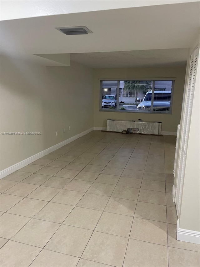 empty room with radiator heating unit, light tile patterned floors, baseboards, and visible vents