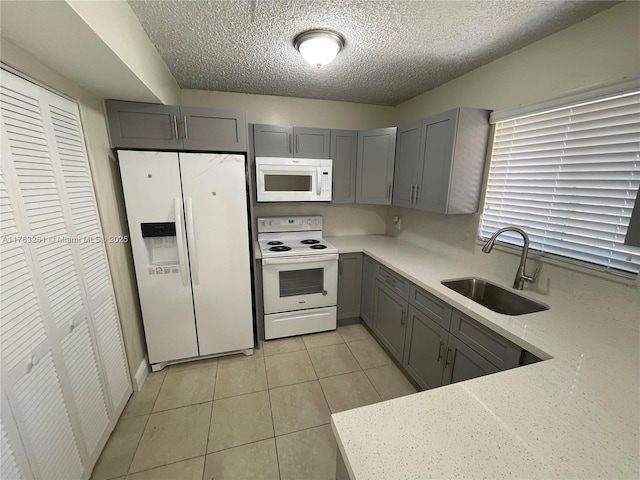 kitchen with gray cabinetry, light tile patterned floors, white appliances, a textured ceiling, and a sink