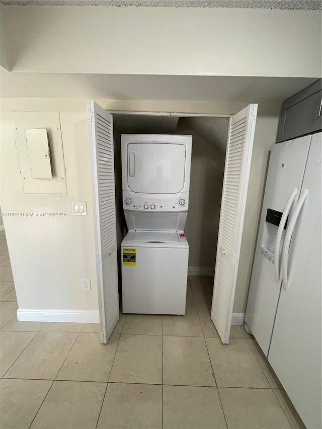 washroom with laundry area, stacked washer and dryer, light tile patterned floors, and baseboards