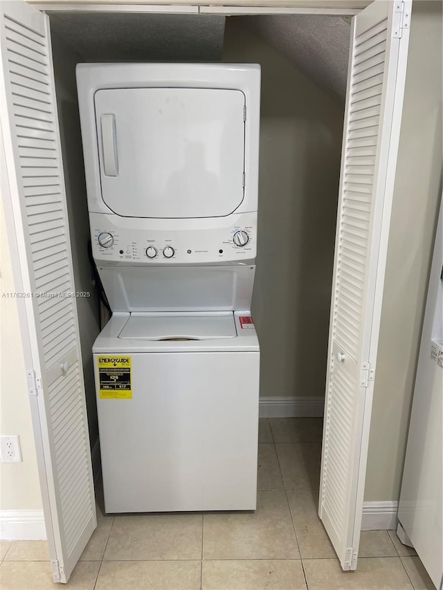 laundry room with light tile patterned floors, baseboards, stacked washer and clothes dryer, and laundry area