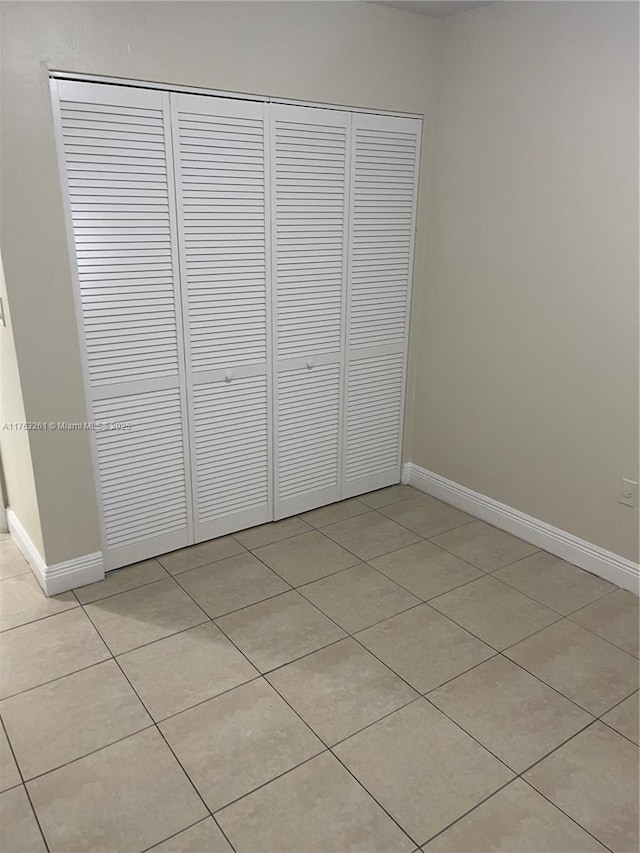 unfurnished bedroom featuring light tile patterned floors, baseboards, and a closet