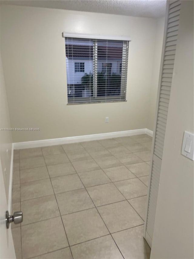 spare room featuring light tile patterned floors, a textured ceiling, and baseboards