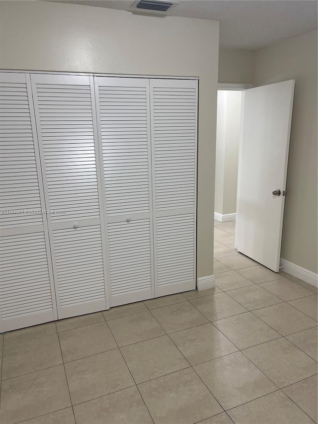 unfurnished bedroom featuring visible vents, light tile patterned floors, baseboards, and a closet