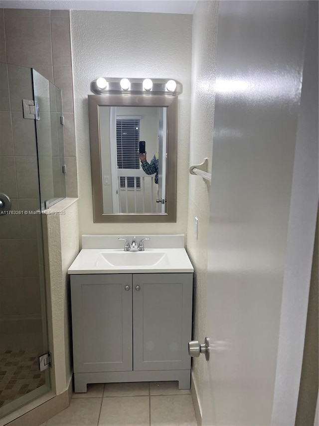 bathroom with tile patterned flooring, a shower stall, vanity, and a textured wall