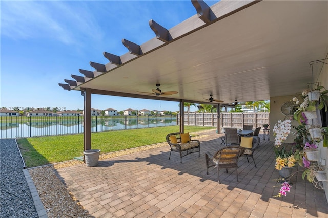 view of patio / terrace with a ceiling fan, fence, and a water view