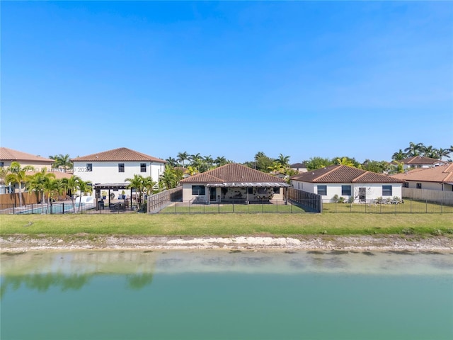 back of property featuring fence, a water view, and a lawn