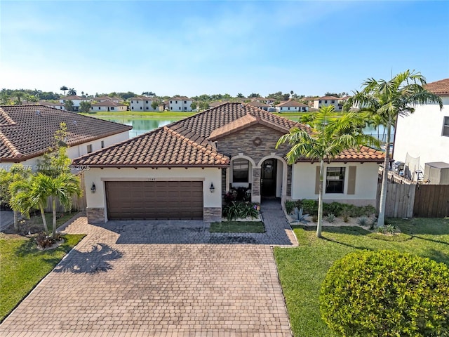 mediterranean / spanish home featuring stucco siding, decorative driveway, stone siding, fence, and an attached garage