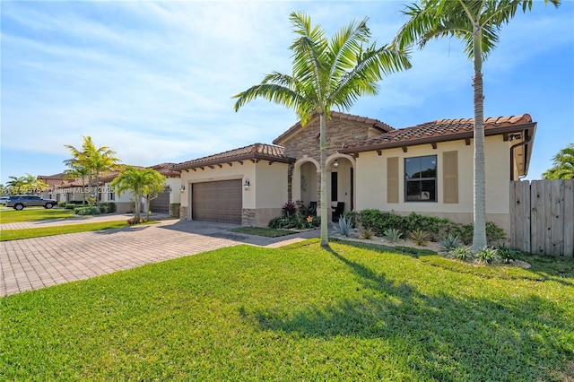 mediterranean / spanish-style house with stucco siding, a front lawn, a garage, a tile roof, and decorative driveway