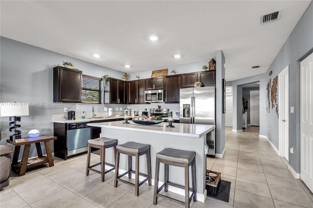 kitchen with a sink, dark brown cabinetry, light countertops, appliances with stainless steel finishes, and a kitchen bar