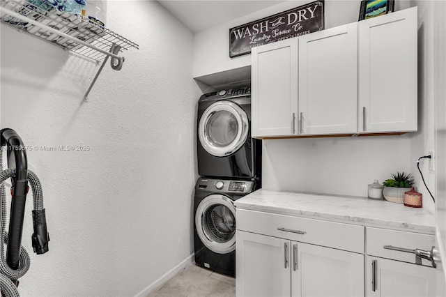 laundry area with baseboards, cabinet space, stacked washer and clothes dryer, and a textured wall