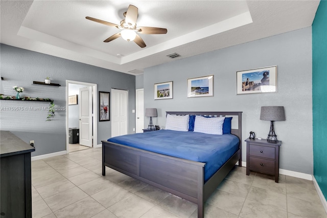 bedroom featuring light tile patterned floors, a ceiling fan, baseboards, visible vents, and a tray ceiling