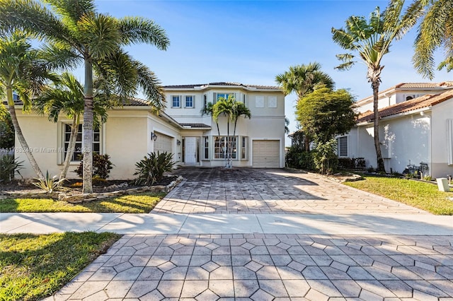 mediterranean / spanish house with a tiled roof, decorative driveway, an attached garage, and stucco siding