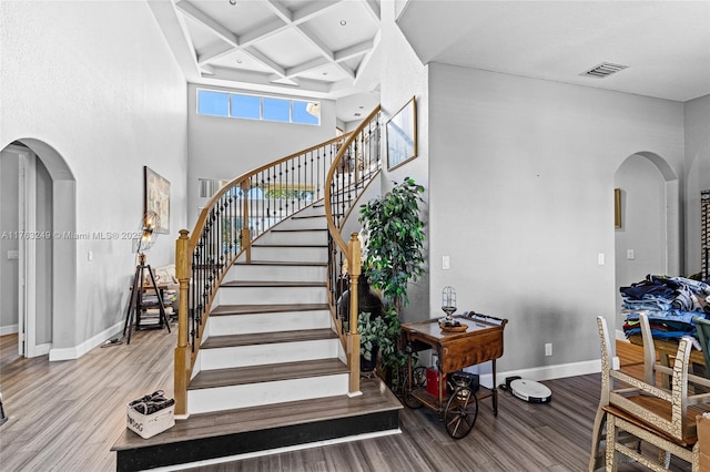 staircase featuring arched walkways, visible vents, coffered ceiling, and wood finished floors