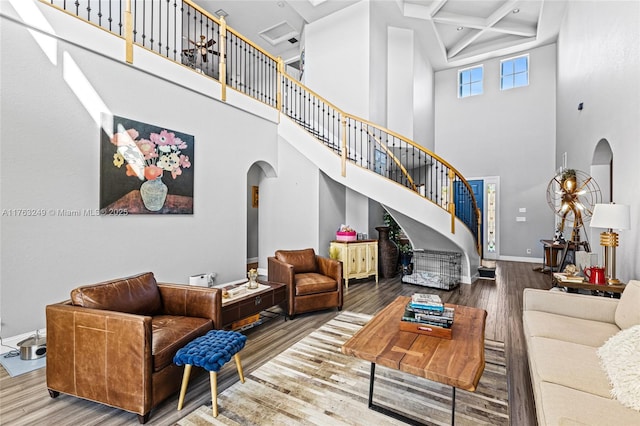 living room with coffered ceiling, wood finished floors, arched walkways, baseboards, and stairs