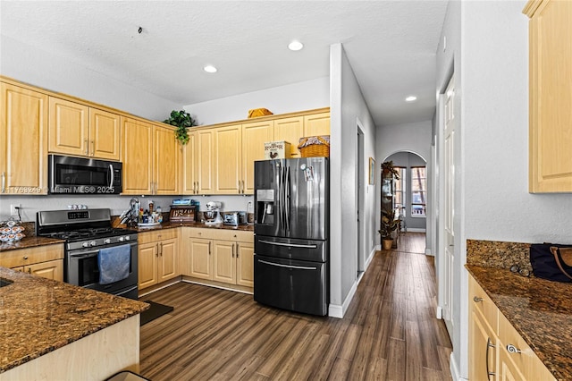 kitchen featuring light brown cabinets, arched walkways, stainless steel gas range, and black fridge