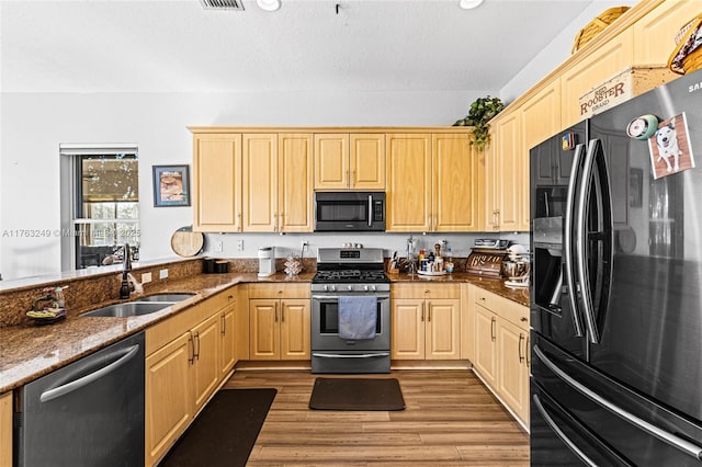 kitchen featuring light wood-type flooring, light brown cabinets, a sink, dark stone counters, and appliances with stainless steel finishes