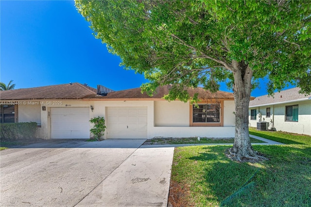 ranch-style home featuring concrete driveway, a front yard, stucco siding, central AC unit, and a garage